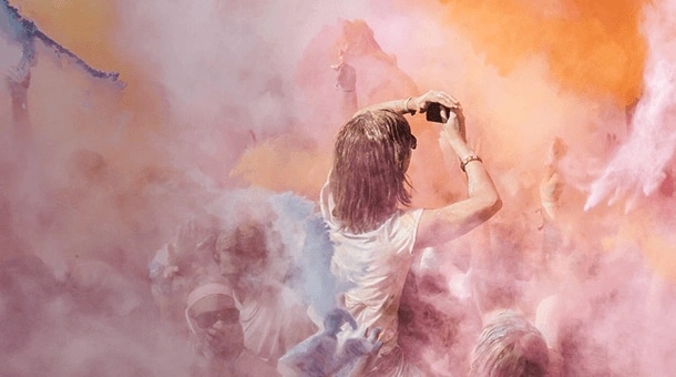 Person taking a selfie in crowd covered by colorful pastel smoke.