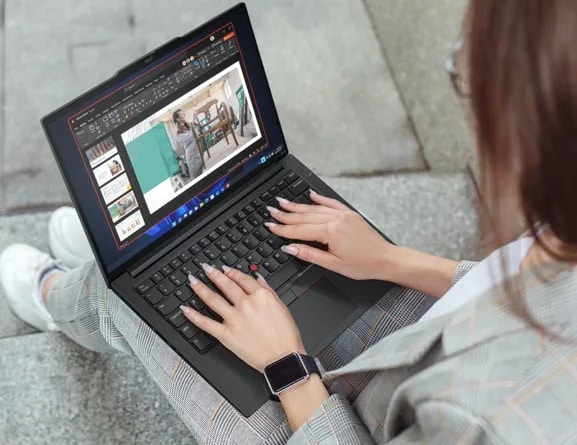 Over-the-shoulder, close-up view of person sitting on concrete stairs, holding ThinkPad E14 Gen 5 (14, intel) laptop in their lap, with both hands on keyboard, looking at slideshow the display