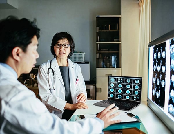 Two doctors looking at medical scan images on a Lenovo ThinkPad P16s Gen 2 (16″ AMD) laptop, opened on desk, as with same images on large monitors