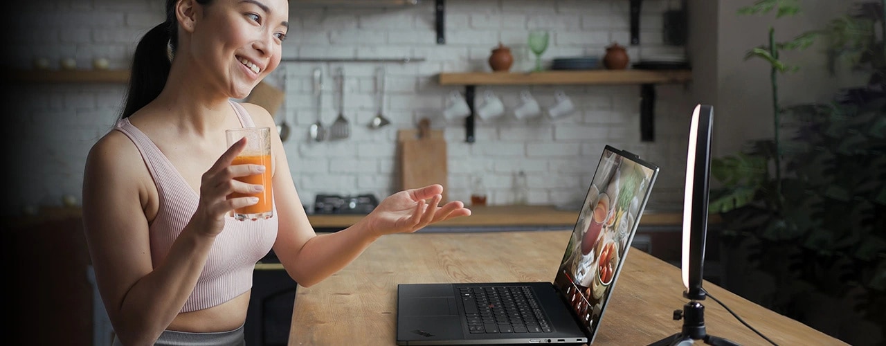 Eine Frau sitzt an einem Tisch mit dem Lenovo Z16 Gen 2 Notebook und einer Lichtquelle und macht ein Video mit der Webcam.