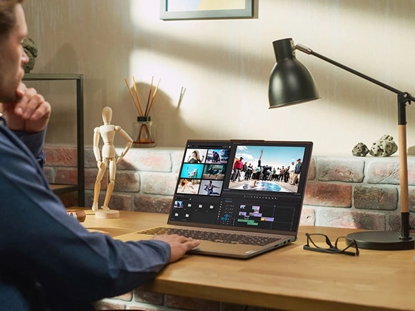 Rear-left side image of a man sitting in his home office and working with a video editing software on the Lenovo IdeaPad Pro Gen 9 16 inch laptop.