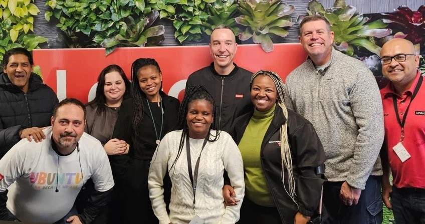 Un groupe diversifié de huit personnes souriant devant un signe Lenovo