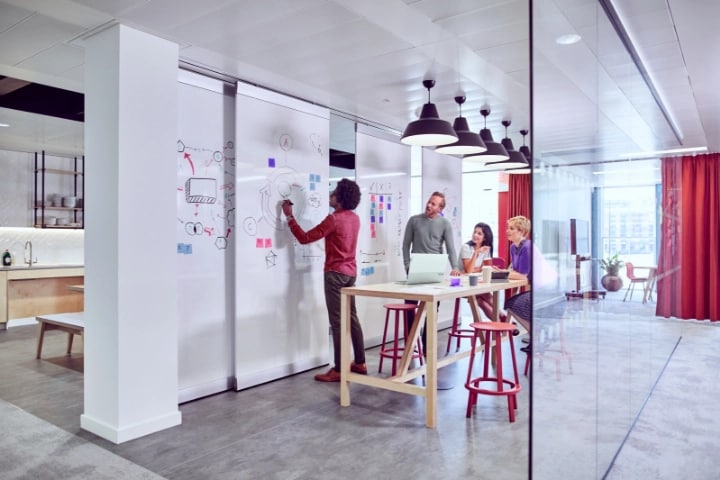 Un equipo de cuatro personas intercambiando ideas en una pared de pizarra blanca