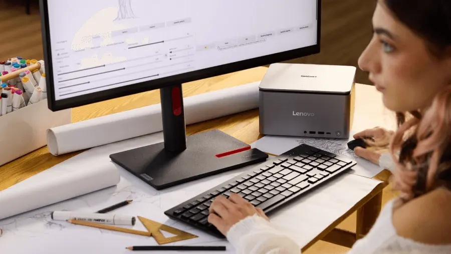Close-cropped view of a person’s face as they intently use a ThinkCentre desktop PC, with various architectural drawings and tools strewn about their desk.