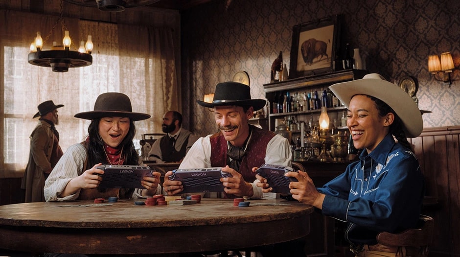 Three people in cowboy attire play games with Legion Go S’s at a wooden table.