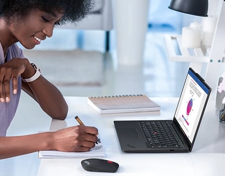 A woman at a desk takes notes in front of a ThinkPad X13 Gen 6 (13” AMD).