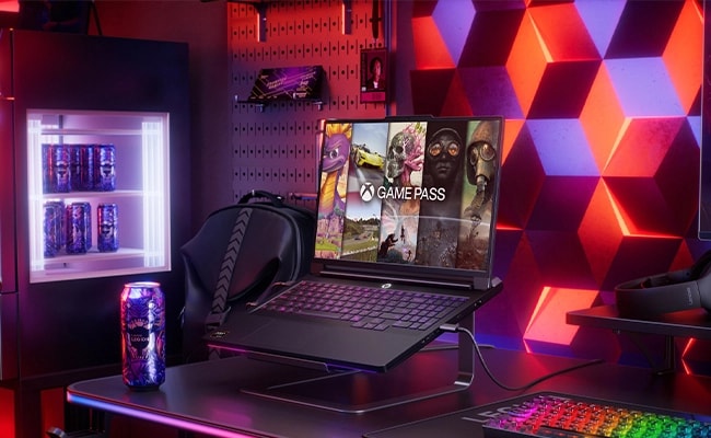 The Lenovo Legion Pro 7 Gen 10 (16” AMD) with an Xbox Game Pass UI on the display, against a colorful background that includes a mini-fridge, monitor, and keyboard. מחשב נייד Legion Pro 7 16AFR10H 83RU001RIV מבית Lenovo