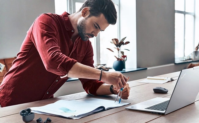A man at a desk wields a compass as he looks at a Lenovo ThinkPad laptop.
