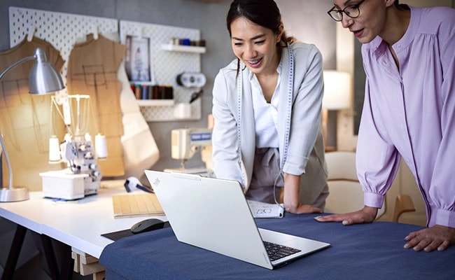 Two women in a fashion environment look at a Lenovo ThinkPad laptop.