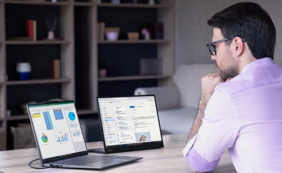 A man at a desk looks at two Lenovo ThinkPad 2-in-1 laptop in different use modes.