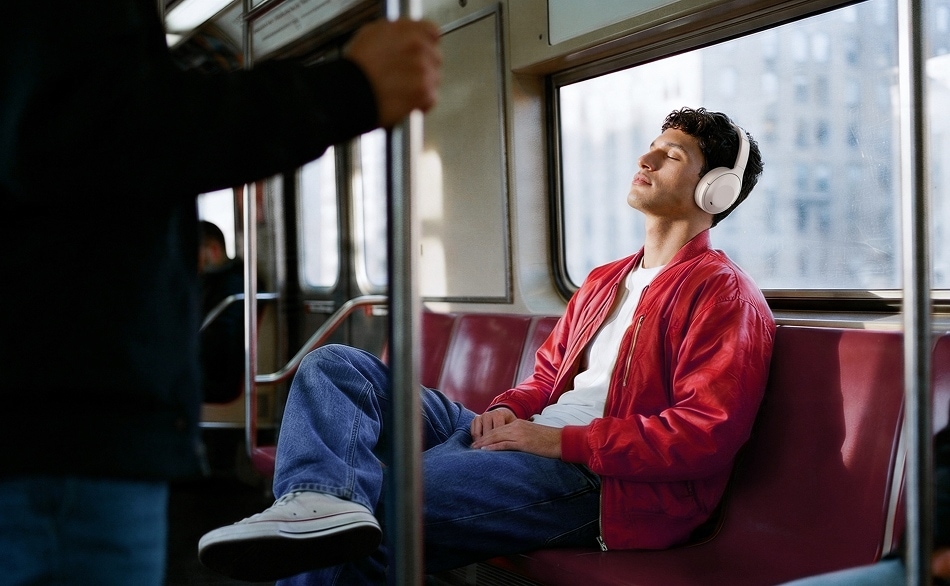 A man wearing white over-ear headphones relaxes with closed eyes on a subway train.