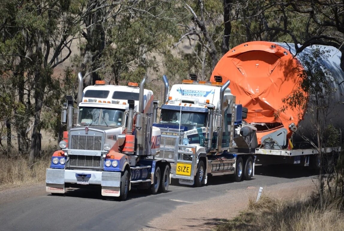 trucks hauling a large pipe down the road