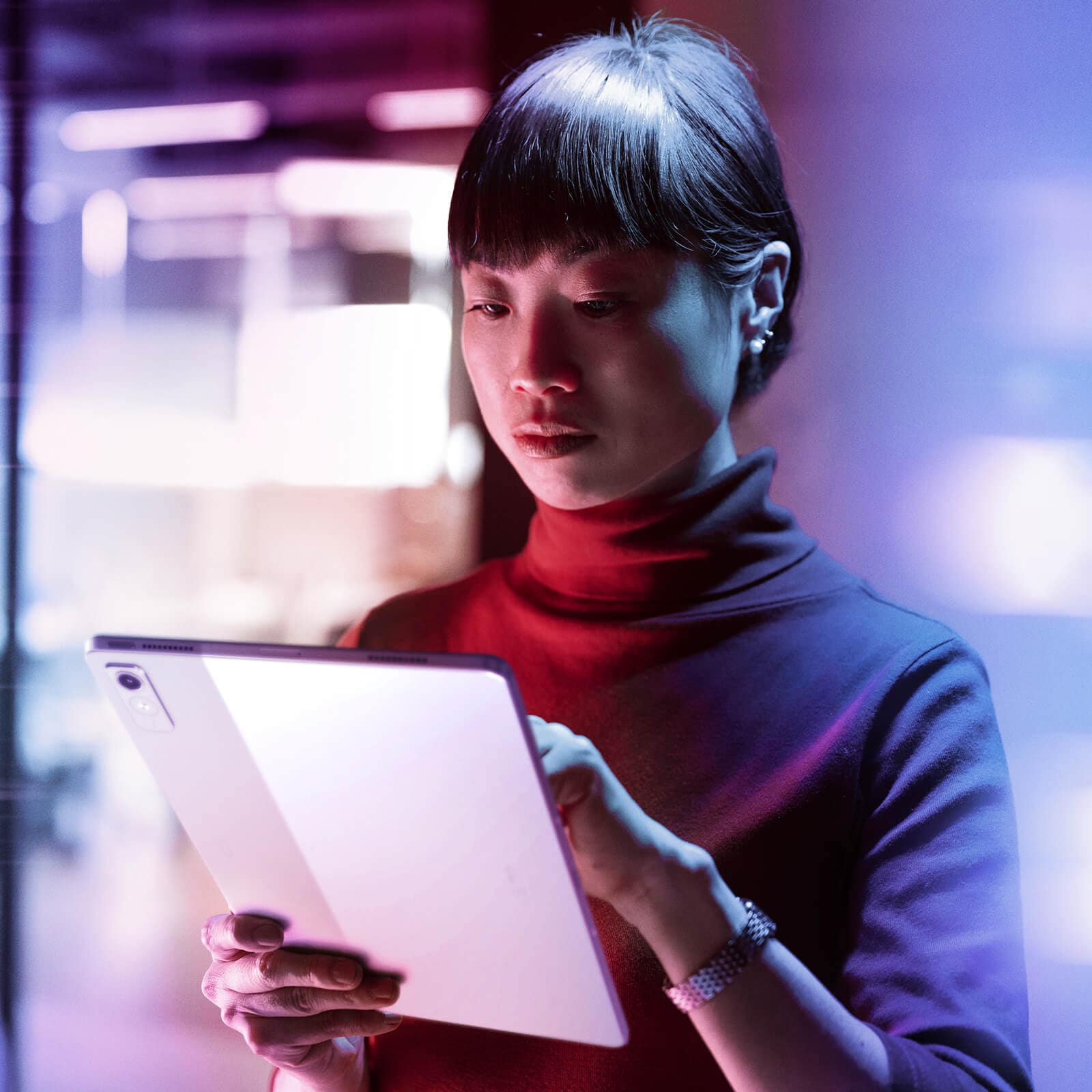 woman using a tablet computer in a modern, low-light environment with colorful ambient lighting and a professional atmosphere.