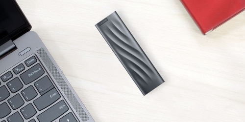 A Lenovo PS8 Portable SSD 512GB is featured next to a laptop on a desk.