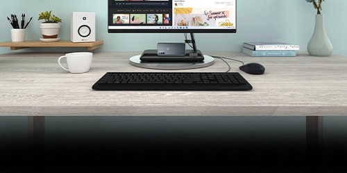 Ordinateur tout-en-un Lenovo placé sur un bureau, avec clavier, souris et une tasse à gauche.