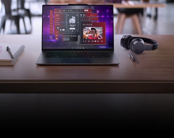 A modern laptop on a wooden desk displaying a vibrant, futuristic user interface with editing and communication tools, including a video call screen showing two people. Next to the laptop are a closed notebook with a pen, a pair of black over-ear headphones, and another pen. The background shows a blurred café-like environment with chairs and tables.