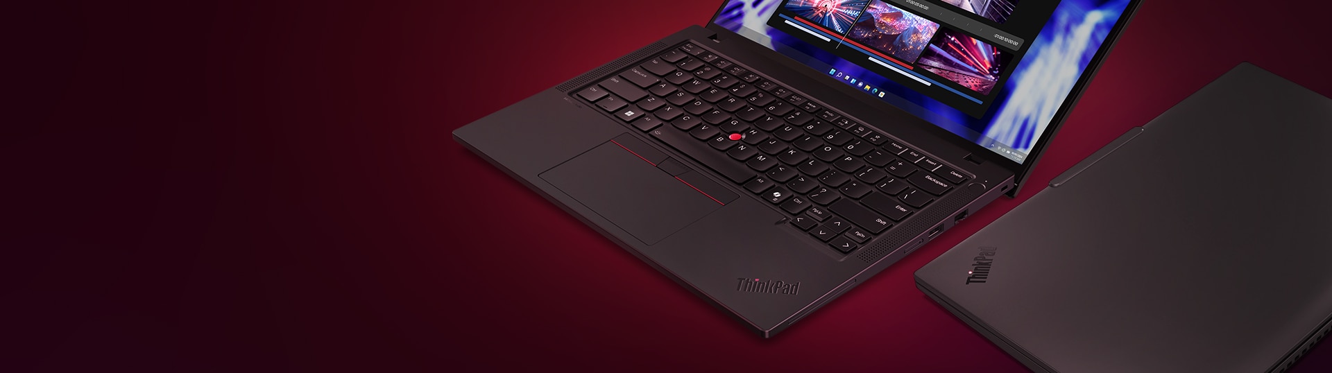Close-up of a Lenovo ThinkPad laptop with its iconic red TrackPoint, black keyboard, and red-accented touchpad, displayed partially open next to a closed unit, against a deep red gradient background. The screen shows a vibrant multimedia editing interface