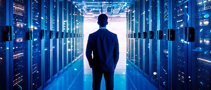 Person standing in a brightly lit data center corridor, surrounded by rows of illuminated server racks. 