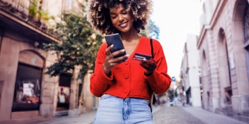Woman with curly hair wearing a red hoodie, holding a smartphone and looking at the screen.