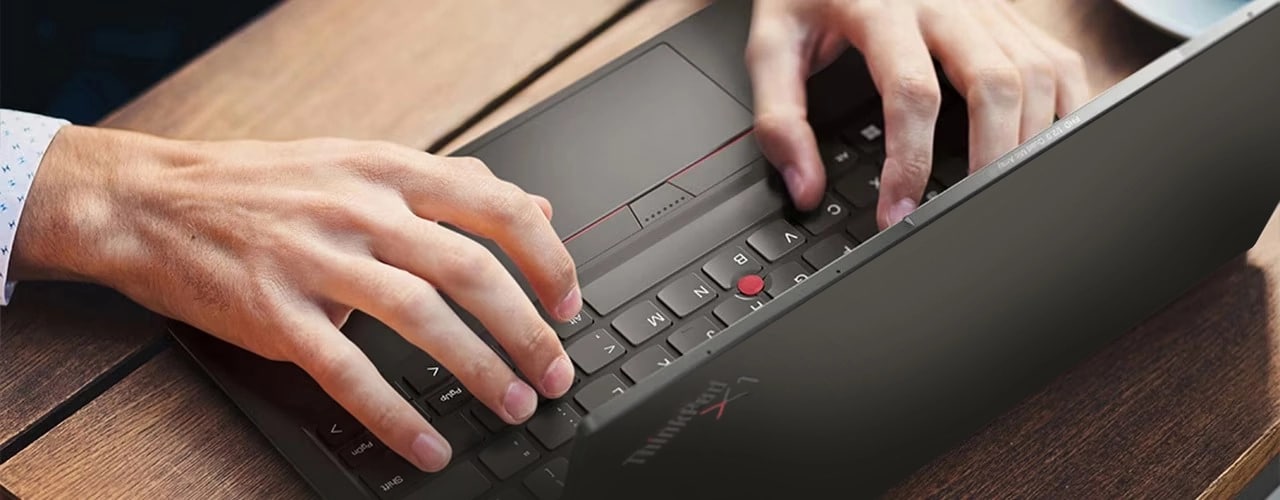Overhead shot of the Lenovo ThinkPad X1 Nano Gen 3 laptop in use on a table, showing the top side of the Communications Bar & hands on the keyboard.