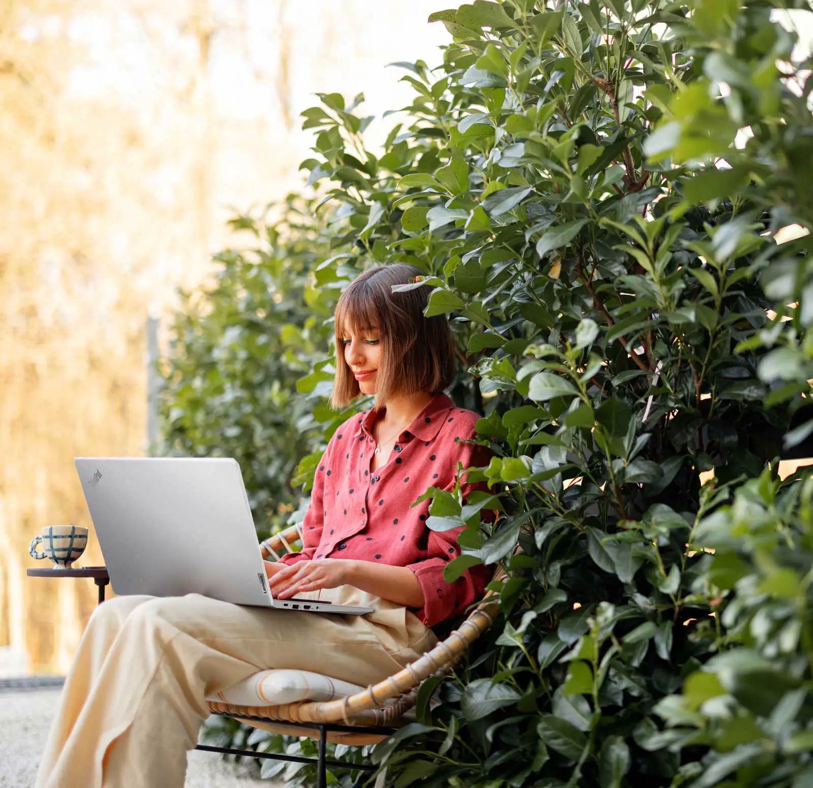 Eine Frau sitzt vor einer Pflanzenwand in einem Garten und arbeitet an ihrem Notebook.