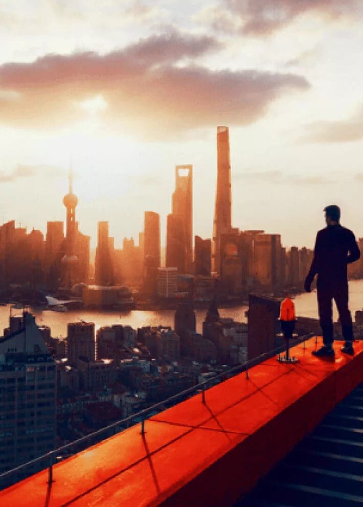 Bărbat în vârful unei clădiri cu vedere spre orizontul orașului la răsăritul zilei.
