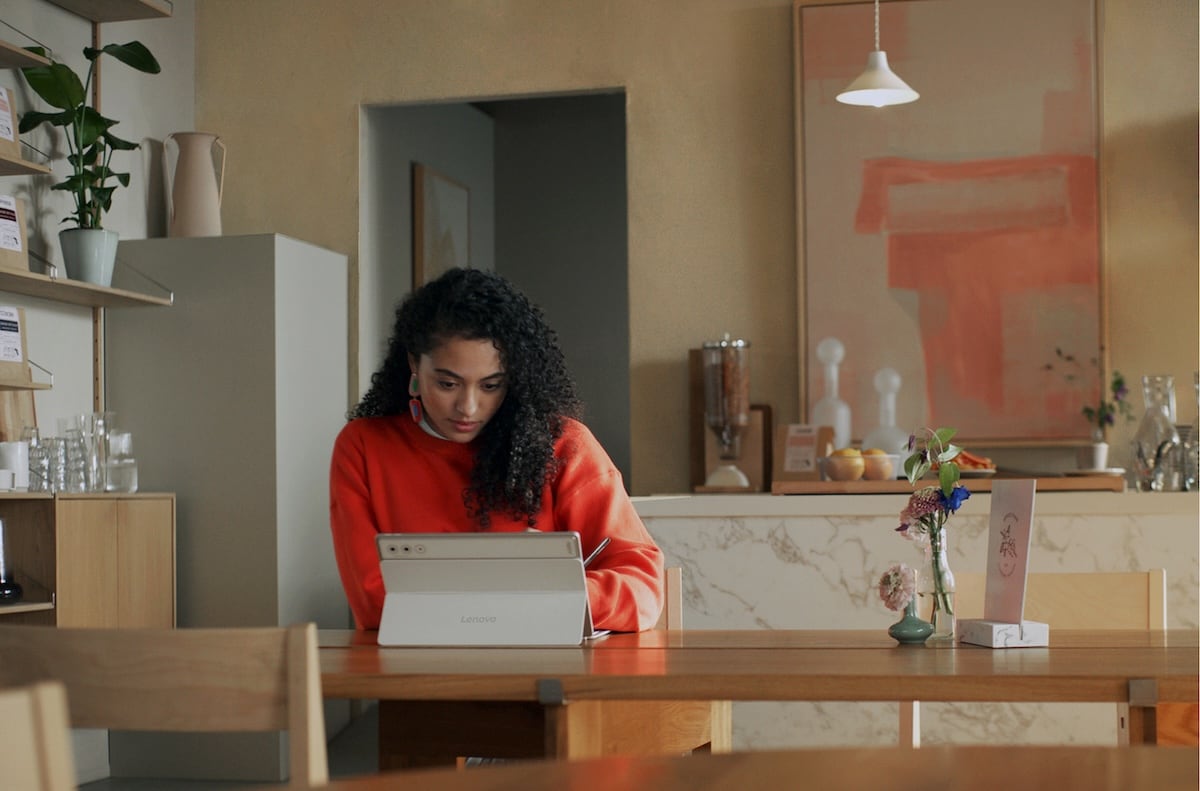 Femme travaillant sur une tablette Lenovo dans un café moderne et convivial, concentrée sur des tâches de productivité avec stylet.