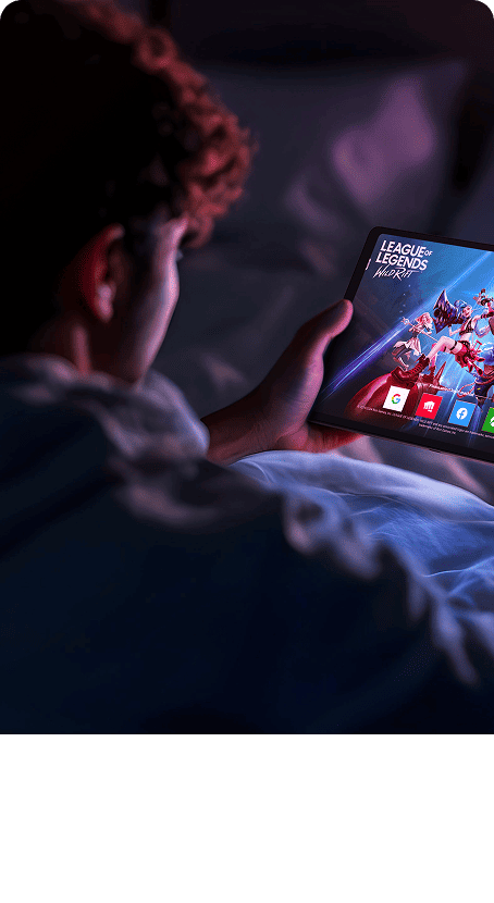 Teen boy gaming on Lenovo Legion Tab in a dark bedroom, with vibrant colors and fast-paced action on screen.