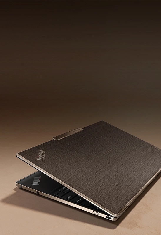 레노버 ThinkPad Z13 Gen 2 노트북 후면이 마주한 상태로 약간 열려 있고 브론즈 알루미늄이 포함된 아마 섬유 상단 덮개가 보이는 모습.