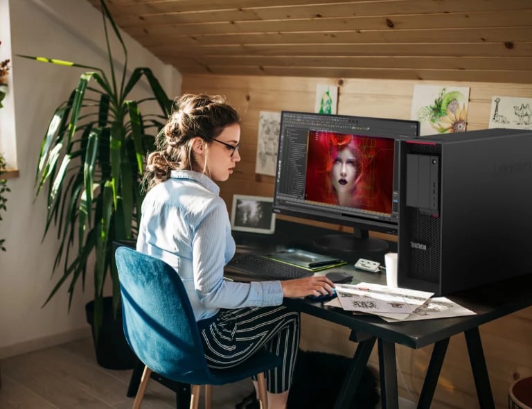 White woman at a desk using the Lenovo ThinkStation P620 tower workstation to create.