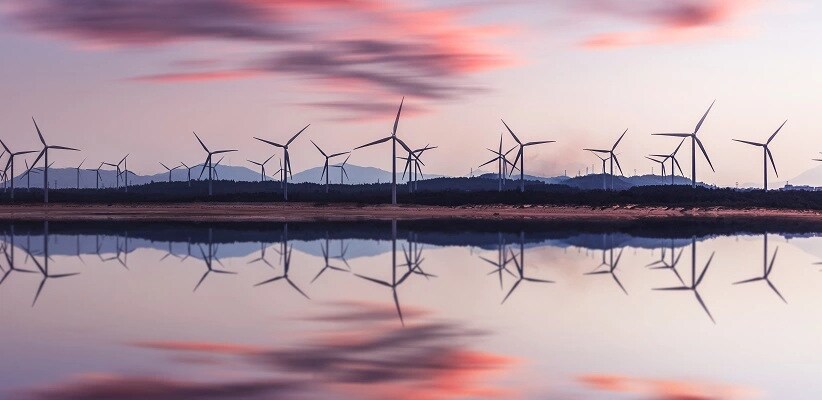 A beautiful Sunset sitting behind windmills lining a lakeside