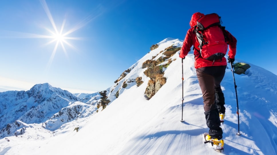 A person in hiking gear climbing a snowy, sunny mountain