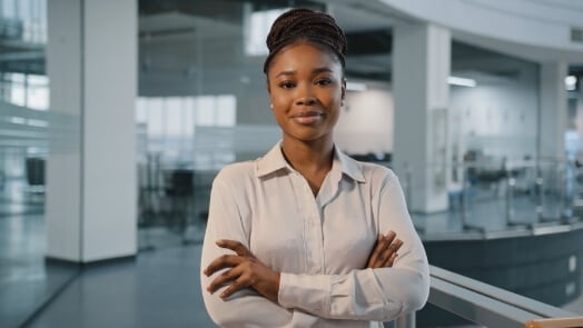 A picture of a young woman looking directly at the camera while standing in the middle of an office space.