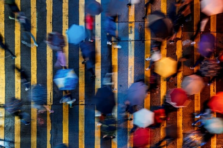 Overhead image of pedestrians holding umbrellas while walking across a busy crosswalk.