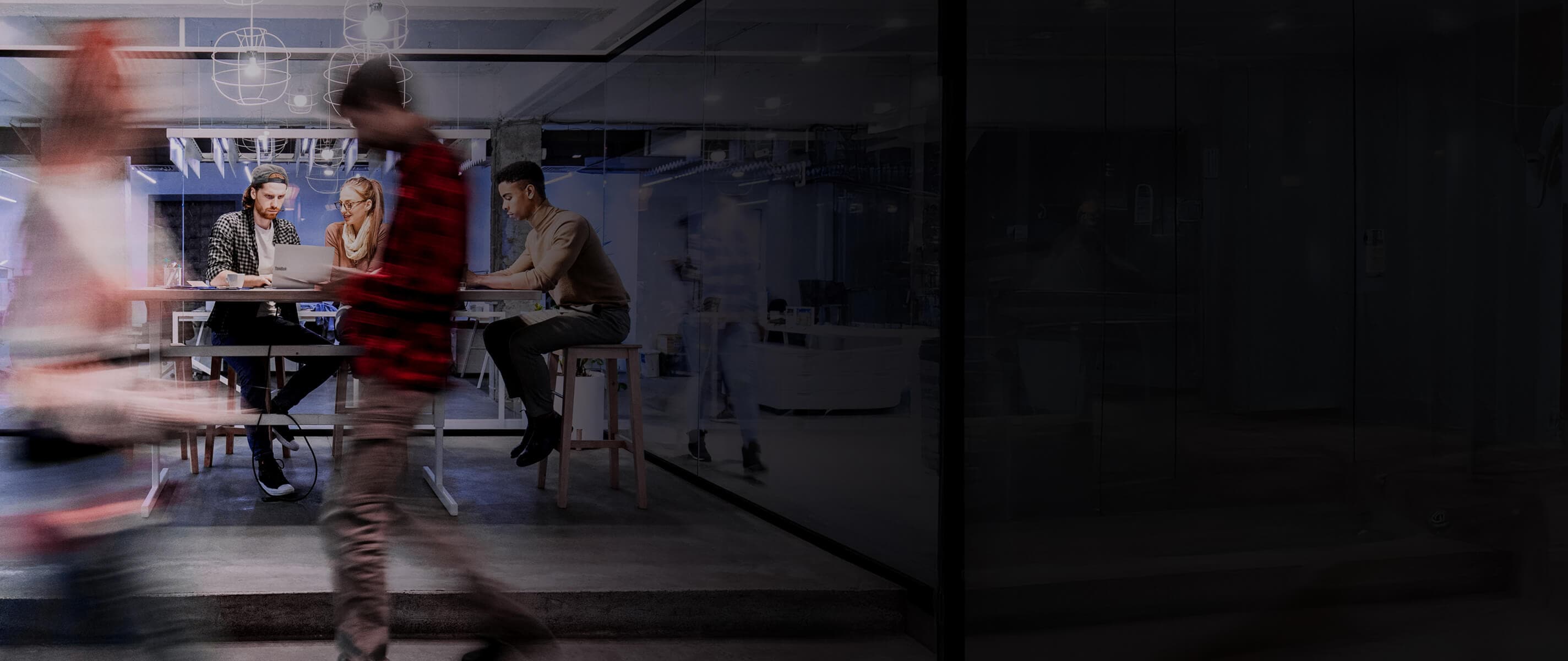 A time lapse of people walking past a conference room with three people working inside on laptops.