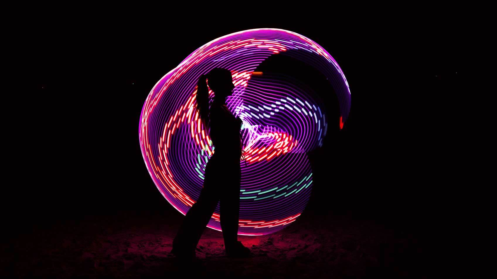 A silhouette of a woman standing in front of purple and red circular light swirls with a black background.