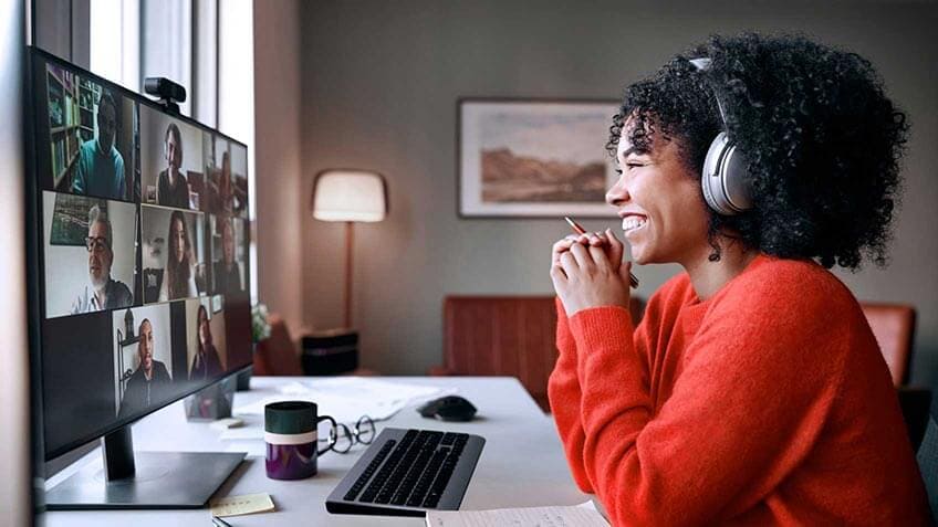 Une femme assise à son bureau, souriant à son ordinateur pendant un clavardage vidéo