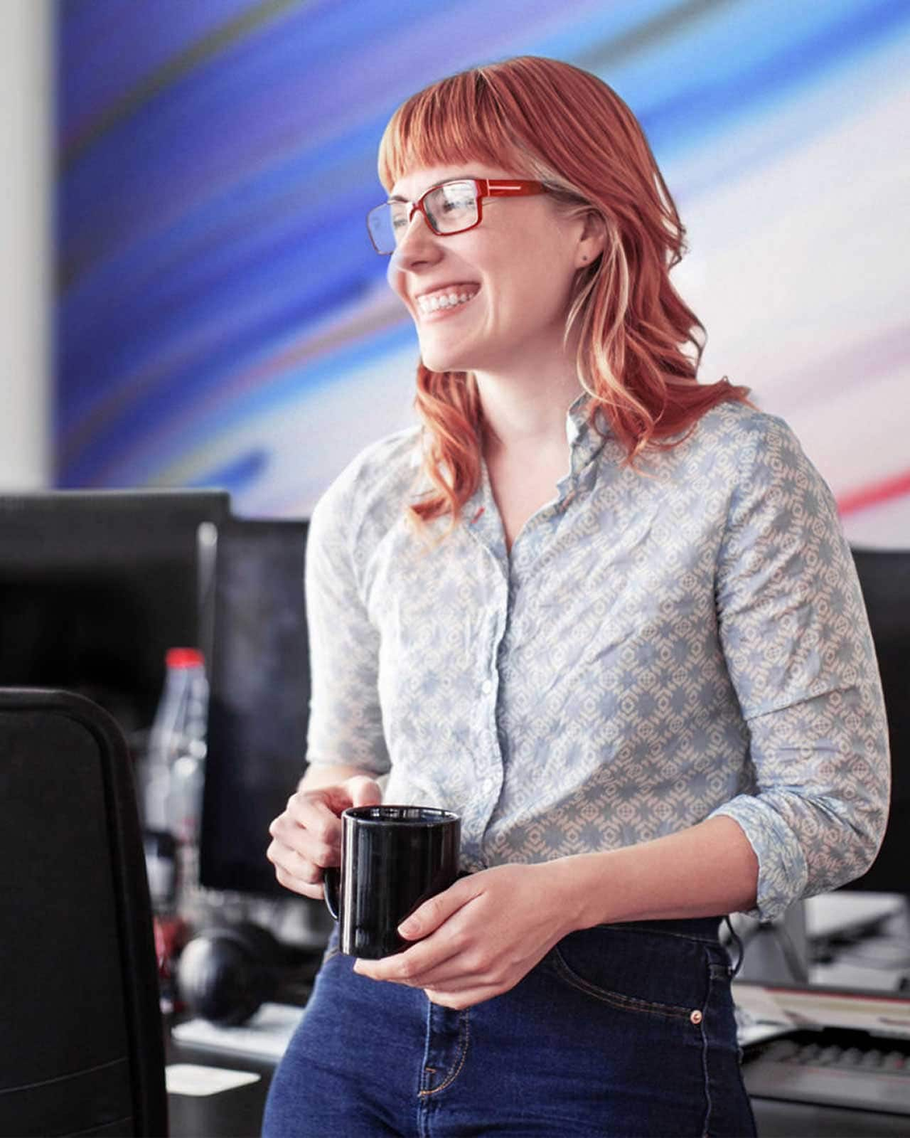 A smiling woman holding a cup of coffee in an office