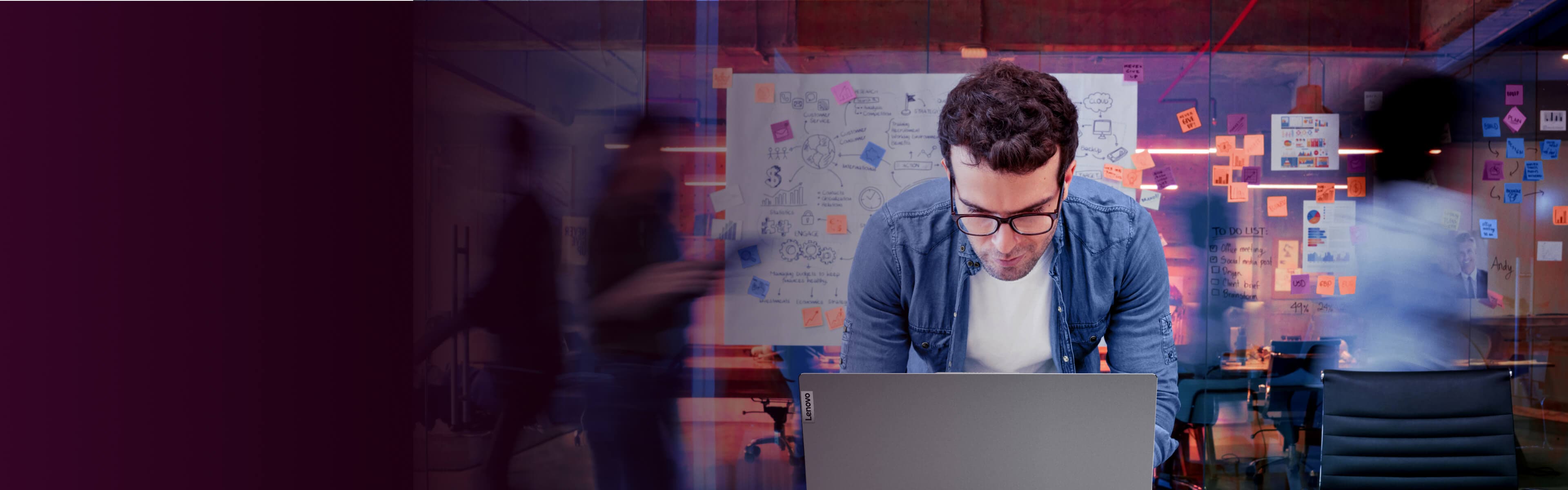 A man leaning over his laptop with notes from a brainstorming session on the wall behind him