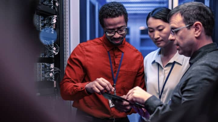 Image of a group of people working together while using a tablet inside a server room. 