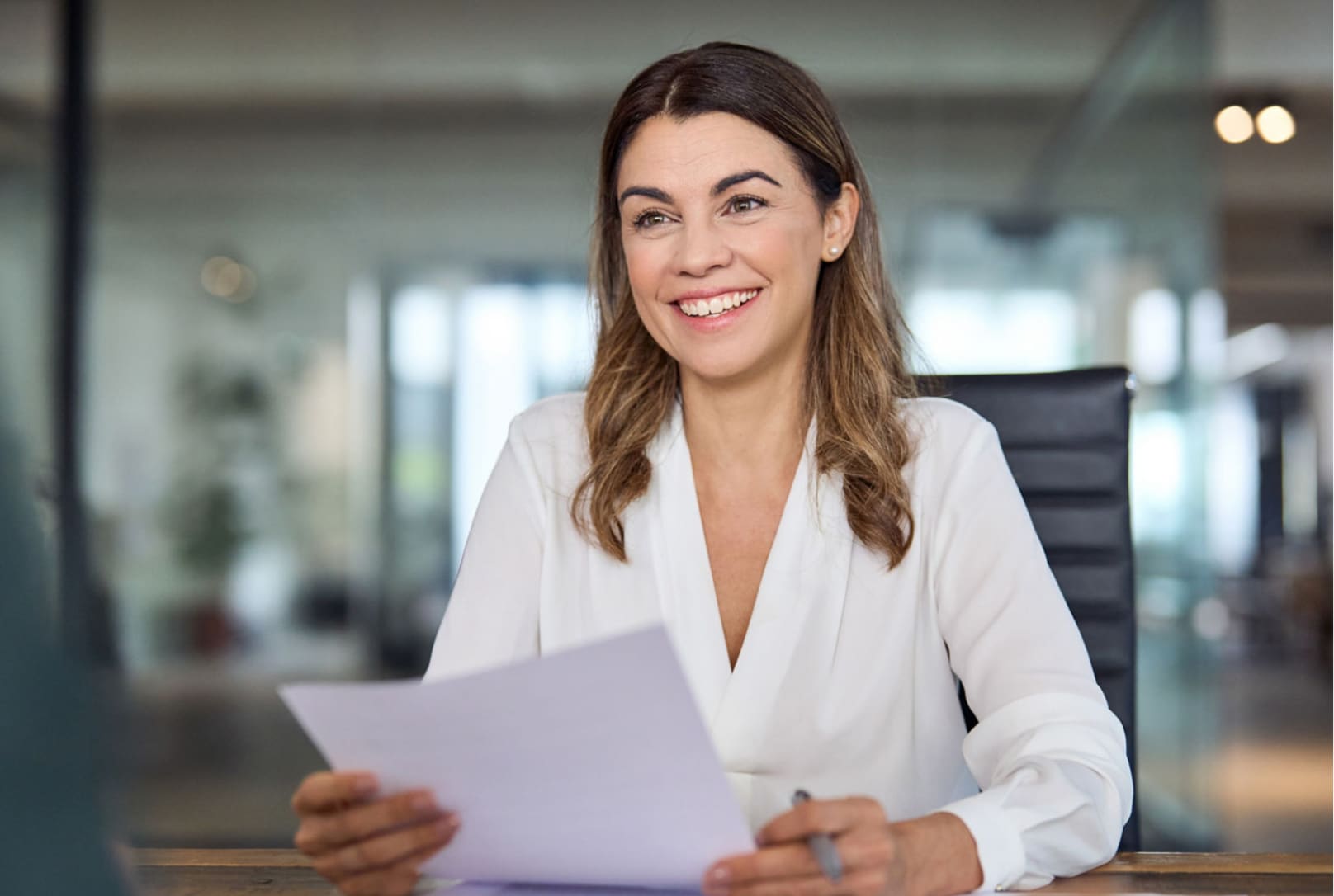 A woman at work holding a piece of paper and a pen and smiling