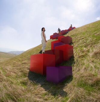 Gens grimpant des cubes rouges et pourpres qui mènent à une colline