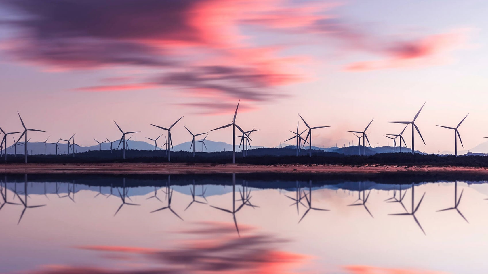 Un parc à éoliennes au crépuscule se reflète dans un étang