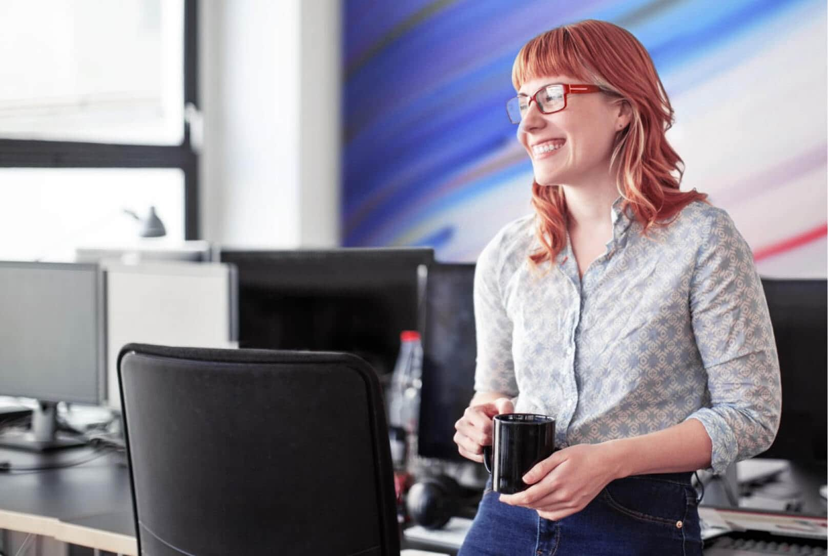 Une femme au bureau, accoudée contre la table de conférence et tenant une tasse de café