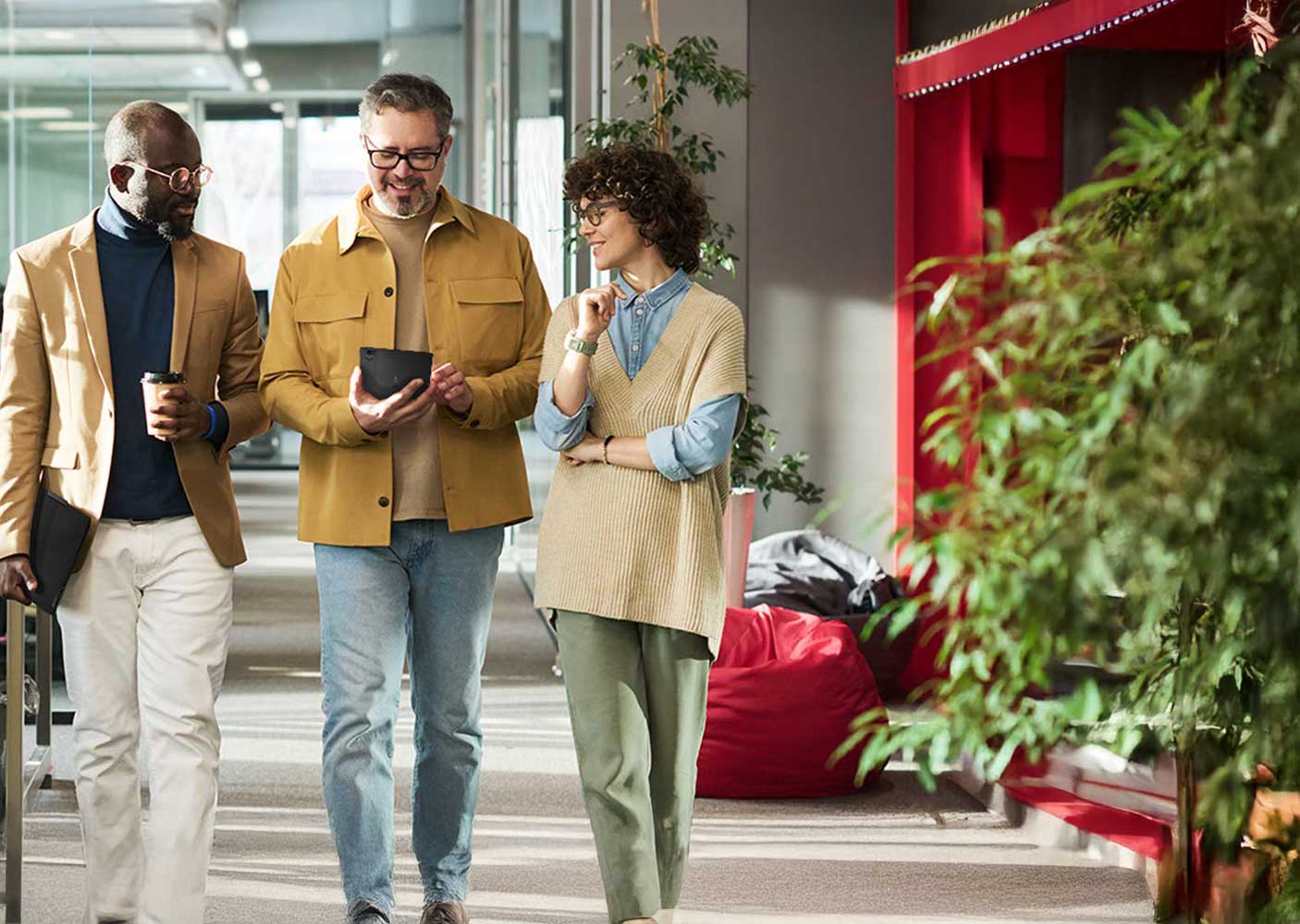 Three colleagues walking down a hallway and looking at a tablet.