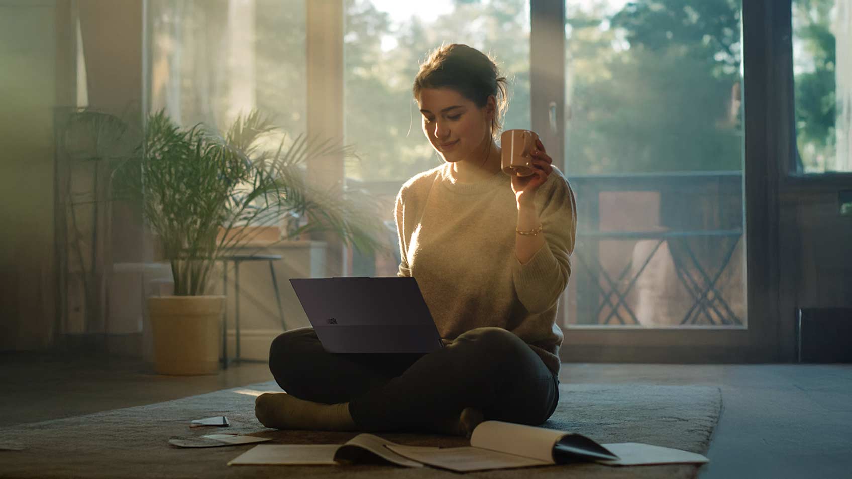 Une femme assise sur le plancher de son appartement et travaillant sur son portable.