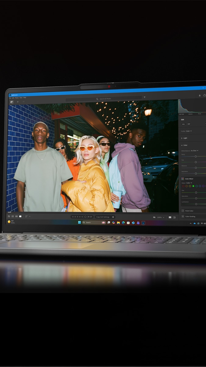 A Lenovo IdeaPad Vibe laptop, lid open, showing an image of five young people in a parking lot outside a club, wearing jackets that emulate five Vibe colors: Radiant Coral, Chill Blue, Zen Green, Dreamy Violet, and Spicy Gold. 