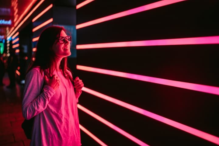 A person with glasses admiring pink neon lights on a modern illuminated wall.