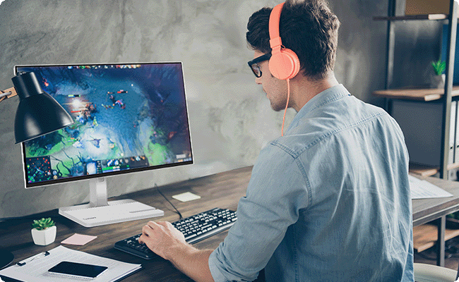 A man with headphones is seated at a desk, working intently on the Lenovo l24d-4c in a modern office environment.