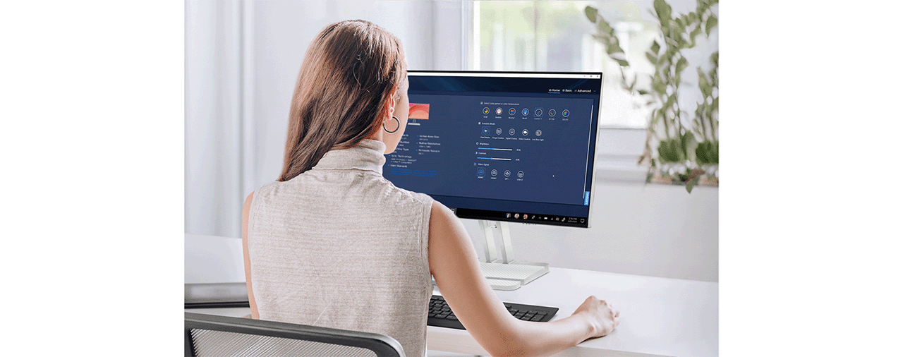 A life-style picture of a woman using the monitor by the window with the  Lenovo Artery (Lenovo Accessories and Display Manager)* software.